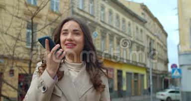 女士使用智能手机语音记录功能在线在城市街道，语音留言。 使用智能手机语音的女孩